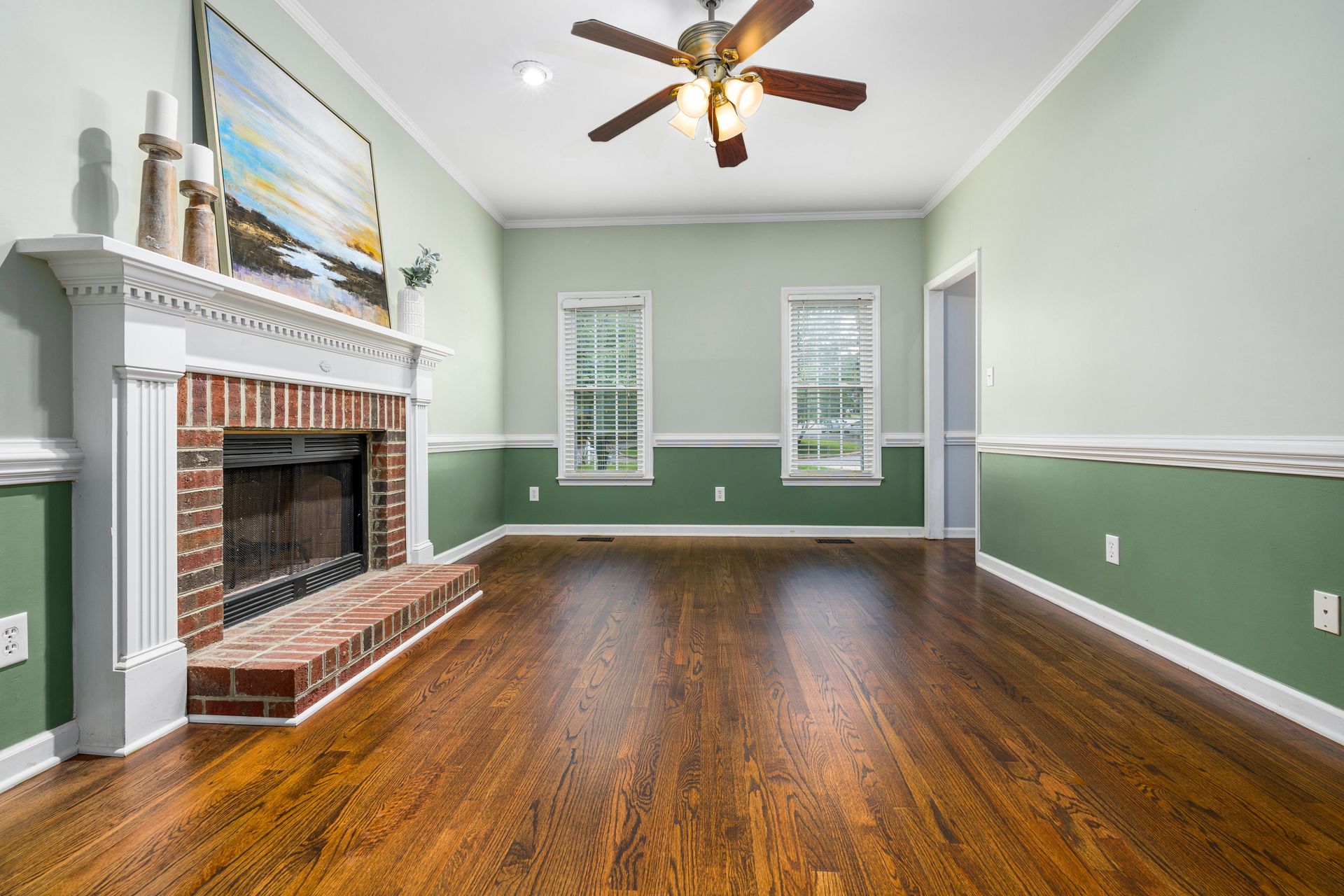 A cozy empty living room featuring a brick fireplace, wooden floors, and elegant decor.